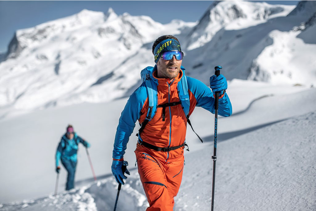 mężczyzna podchodzący na nartach, ma na sobie komplet softshell, na głowie opaskę i okulary przeciwsłoneczne