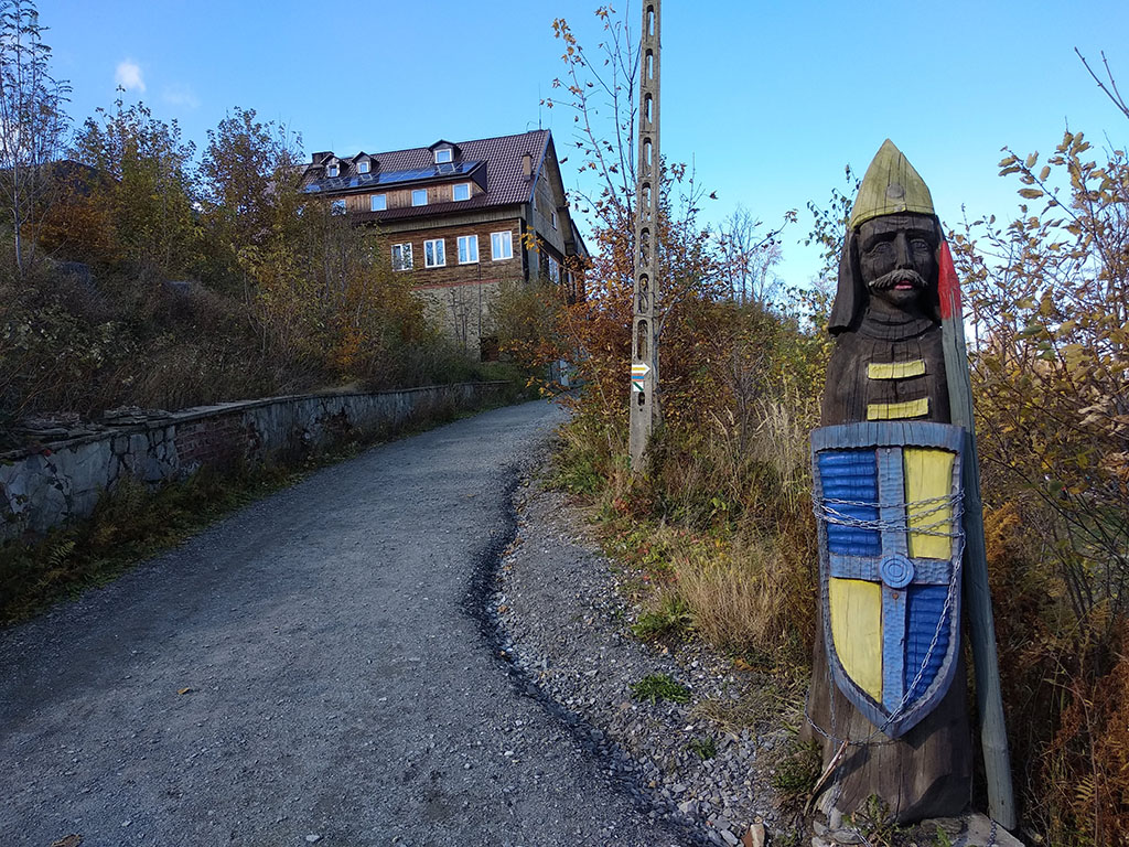 Na pierwszym planie drewniana rzeźba, na drugim schronisko Pod Biskupią Kopą