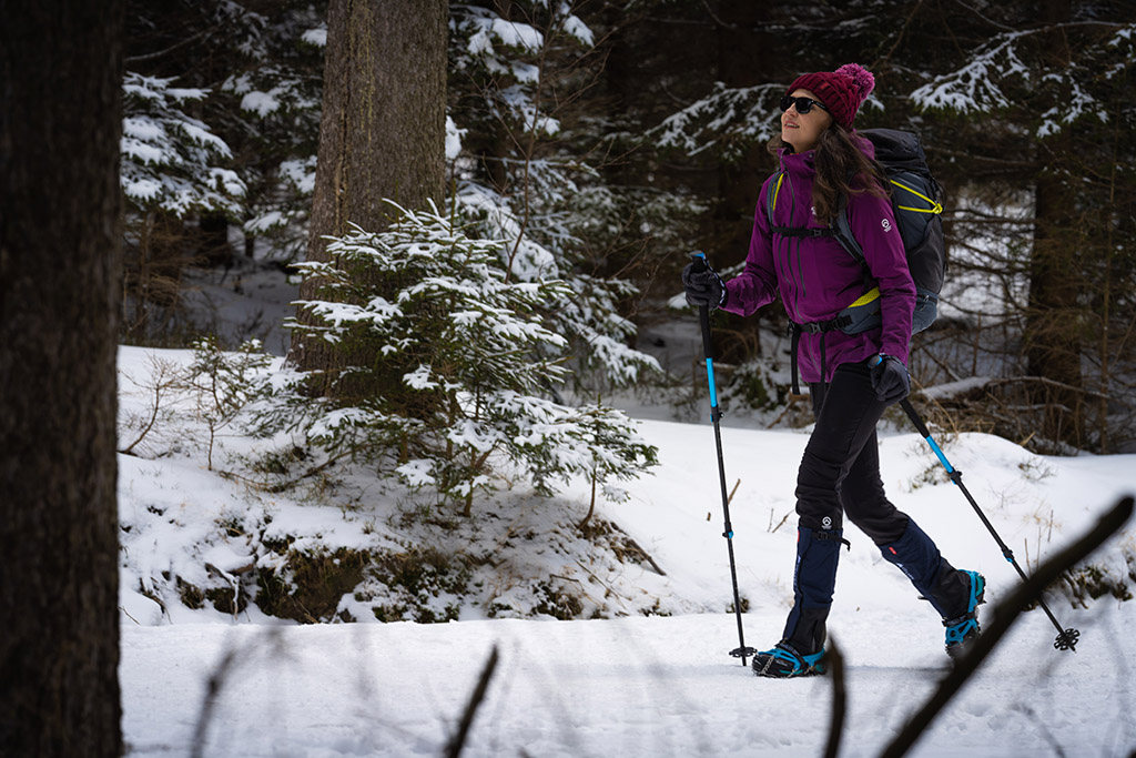 kobieta w lesie ma na nogach raczki a w rękach kije trekkingowe