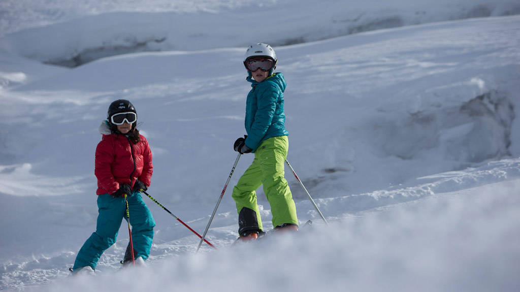 dwoje dzieci na nartach opartych o kije stoi na stoku