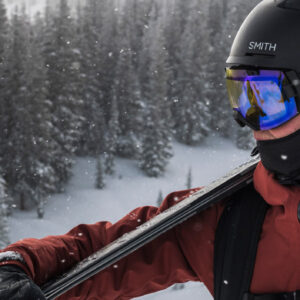 osoba w kasku i goglach trzymająca na ramieniu narty