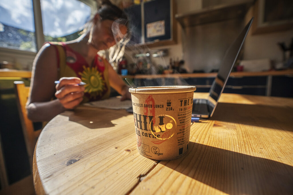 kobieta przy laptopie na pierwszym planie kubek z posiłkiem Lyo Bistro