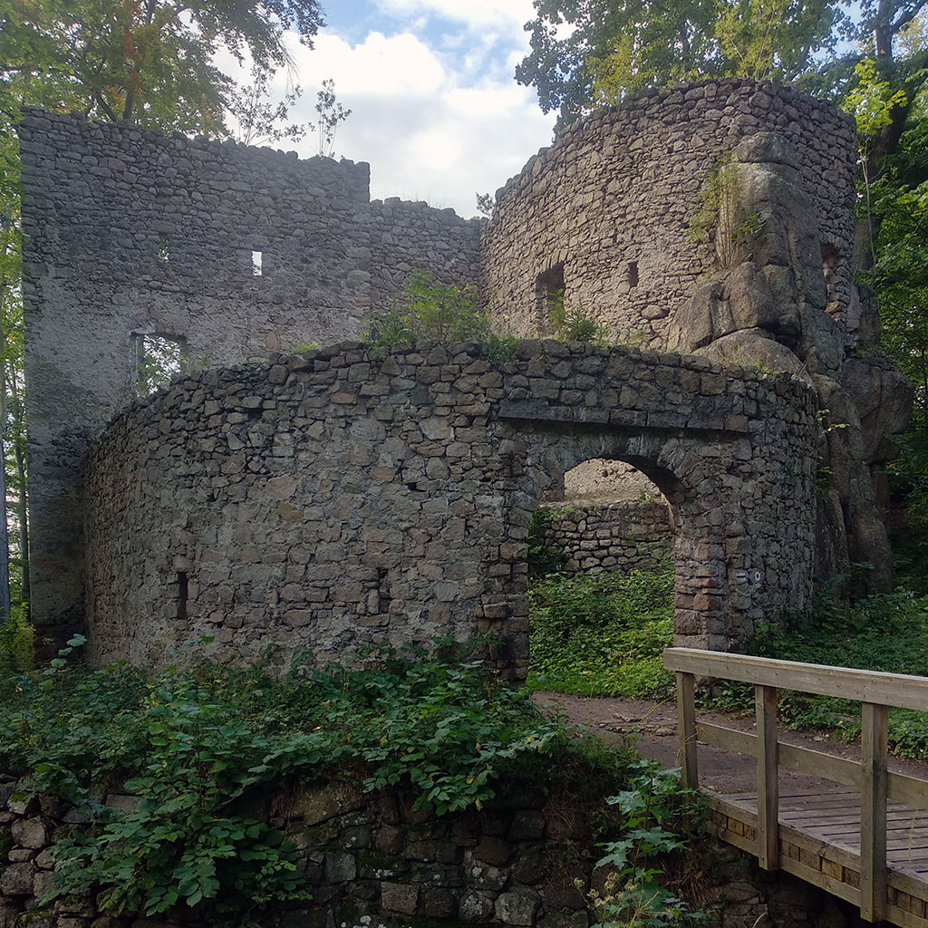 drewniany most a za nim ruiny kamiennego zamku Bolczów