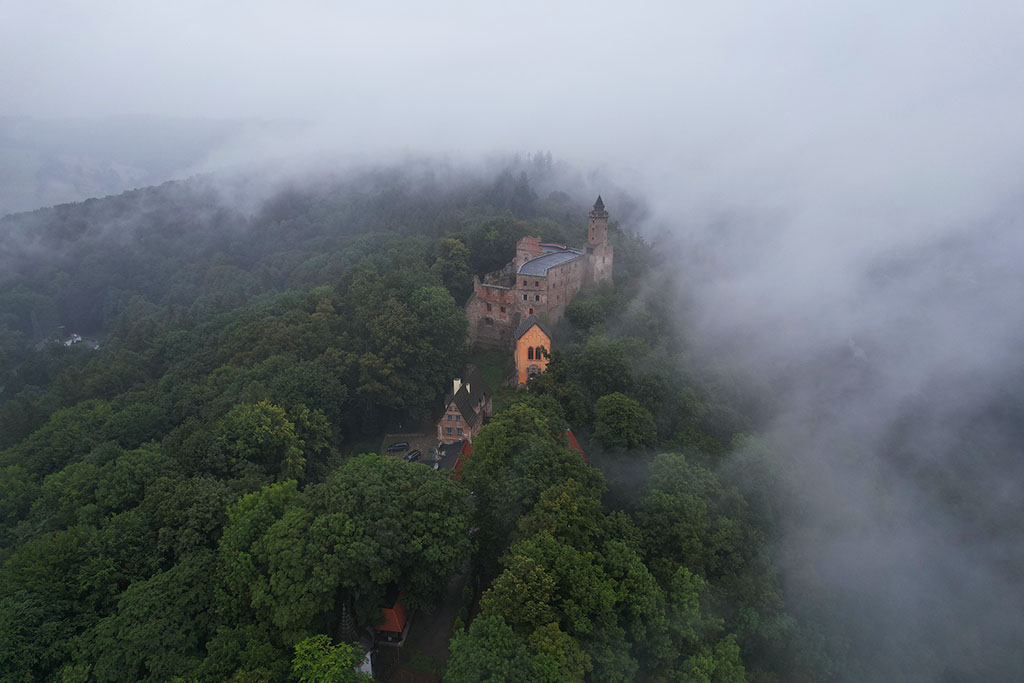 widok z lotu ptaka na zamek Grodno ukryty między drzewami i niskimi chmurami